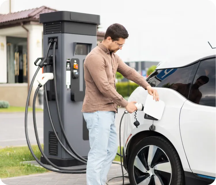 A visitor charges an electric car at a charger outside a residential building